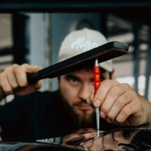 Mechanic expertly repairing car dent using specialized tool in workshop.